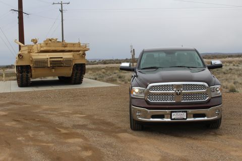2015 Dodge 1500 - A maroon 2015 Dodge 1500 pickup truck is parked on a dirt road, with a military tank visible in the background.