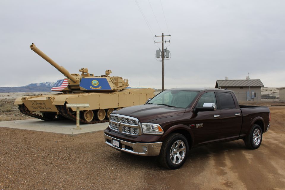 Maroon 2015 Dodge Ram 1500 parked on gravel lot with a tan military tank behind it