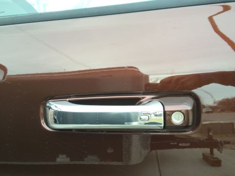 2015 Dodge 1500 - Close-up of a chrome door handle with a keyhole on a brown vehicle, reflecting the surroundings.