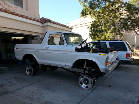 1979 Ford Bronco - A white 1979 Ford Bronco is parked in a driveway with its hood open and missing front wheels.