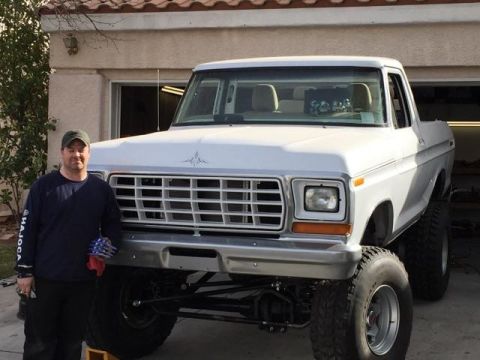 1979 Ford Bronco - A man stands next to a lifted 1978 Ford F-150 pickup truck with a prominent chrome grille.