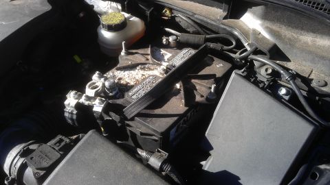 1994 Ford Bronco - Close-up view of a car battery and surrounding engine bay components, showing some corrosion.