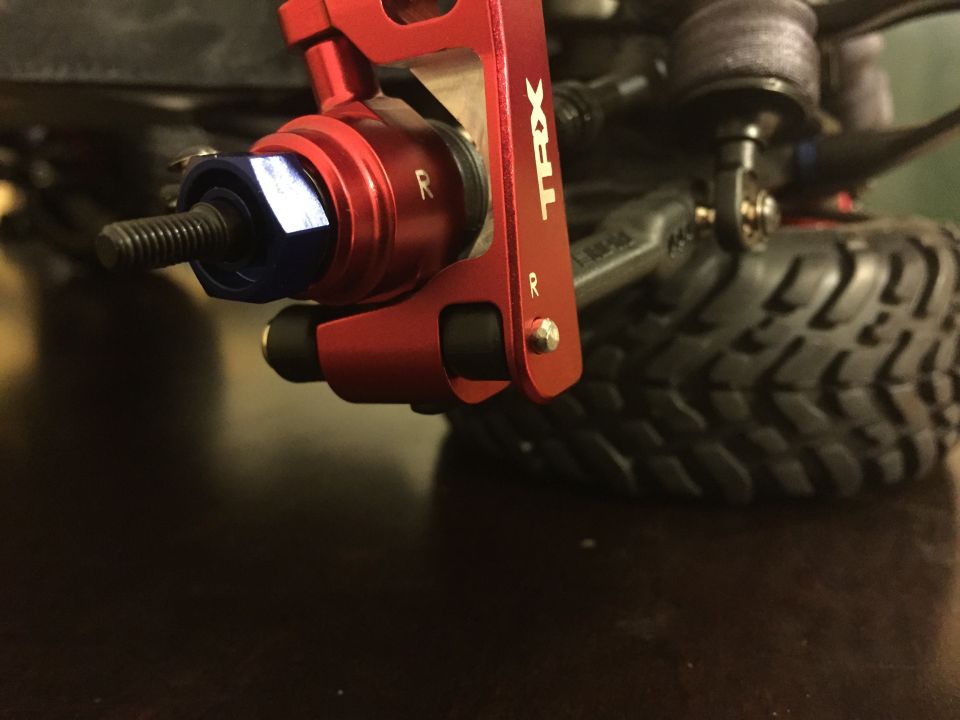 Red TRX suspension component with blue nut and threaded bolt, next to a tire