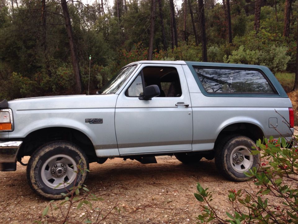Side view of a light blue 1996 Ford Bronco with a dark green top parked on a dirt road