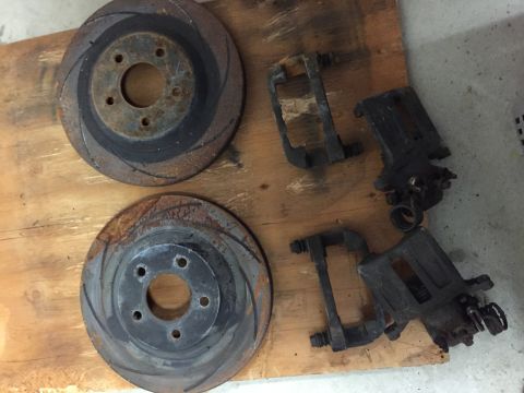 1988 Ford Bronco - Used brake rotors and calipers are laid out on a wooden workbench, showing signs of wear.