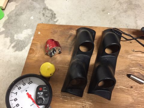 1988 Ford Bronco - Automotive parts, including gauge pods and a tachometer, are laid out on a wooden surface.