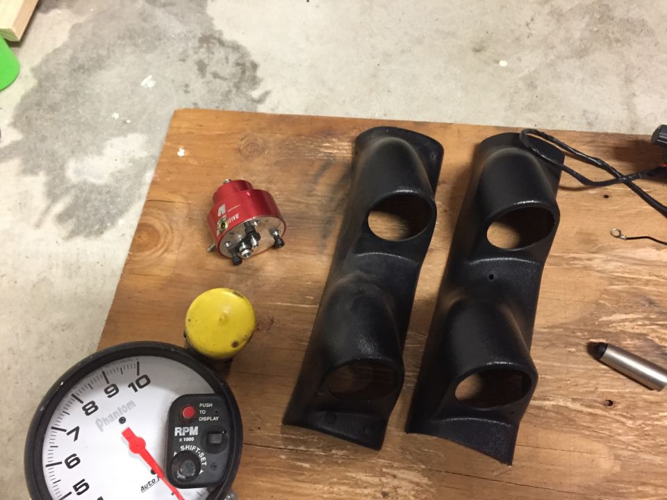 Two black dashboard gauge pods and a red tachometer sit on a wooden surface