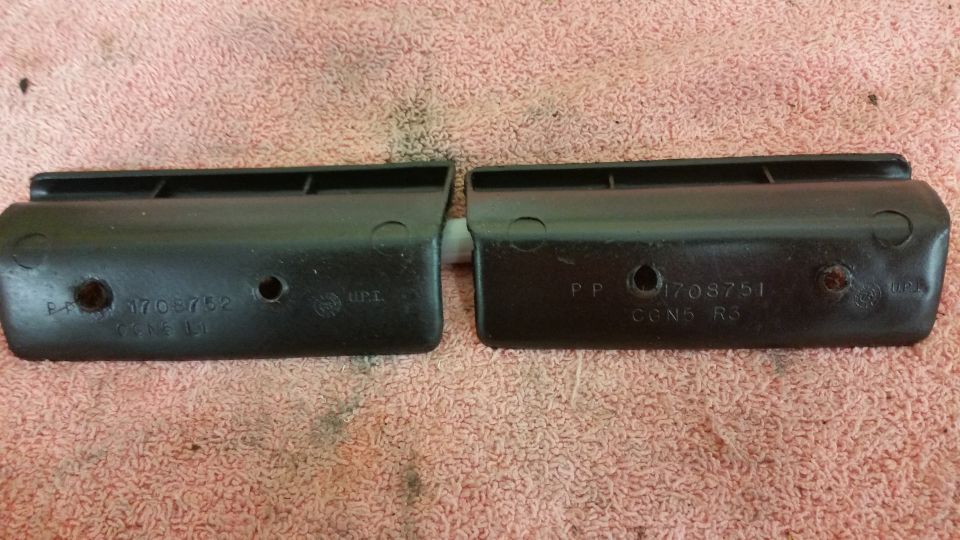 two black plastic automotive parts with numbers stamped on them