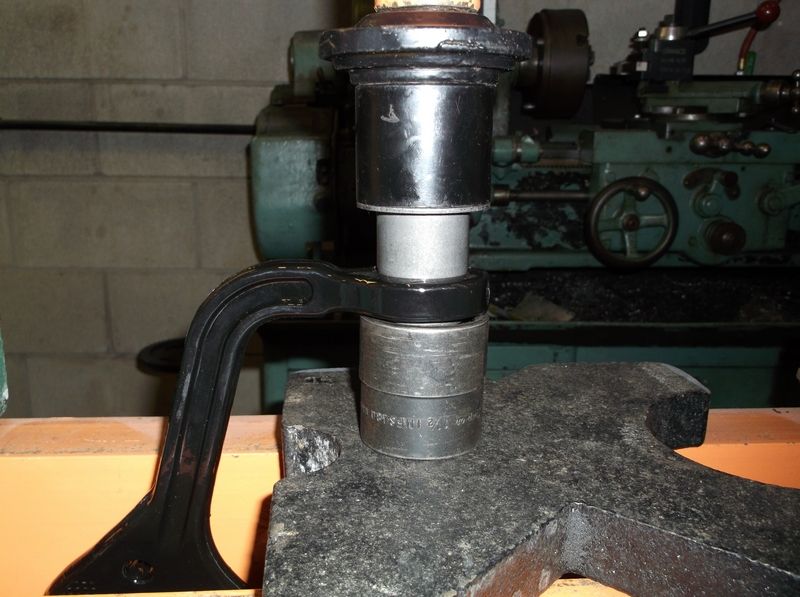 Automotive part being pressed in a vise with a socket and C-clamp, with a metal lathe in the background