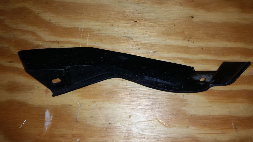 black plastic trim piece with mounting holes, on a wooden surface