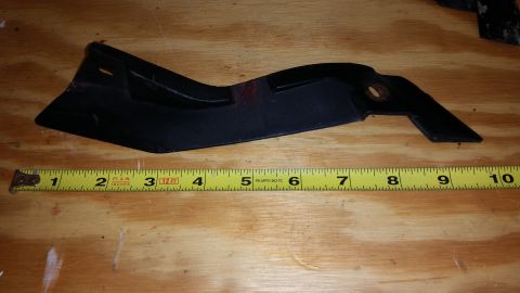 2015 Chevrolet new - A black plastic automotive part is measured with a yellow tape measure on a wooden surface.
