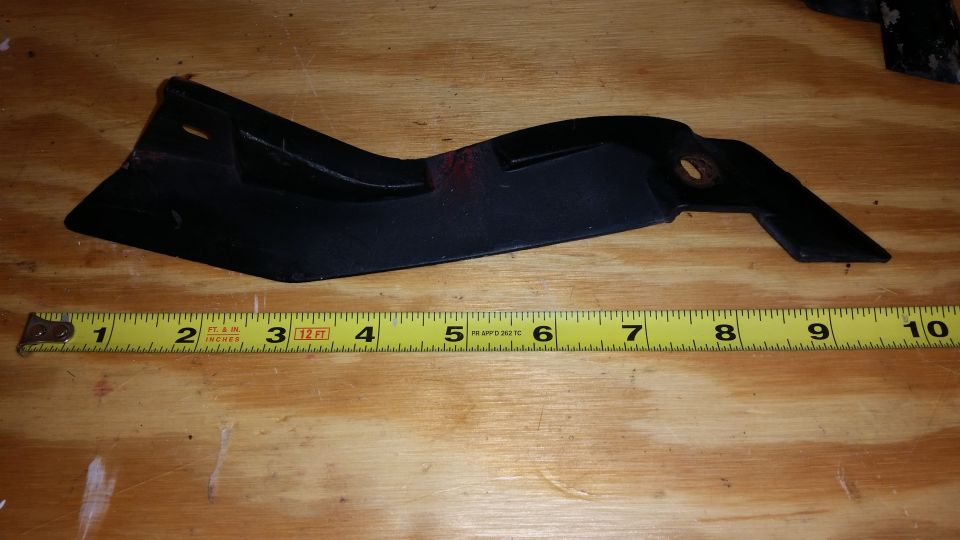 Black plastic automotive part, approximately 10 inches long, with a measuring tape indicating its size