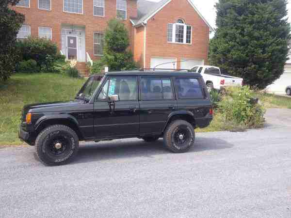 Black SUV parked in front of a brick house with a white pickup truck in the background