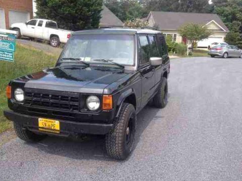 1987 Toyota 4Runner - A black SUV is parked on a gravel driveway, with a white pickup truck visible in the background.