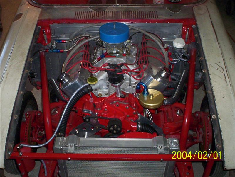Red V8 with blue air cleaner and polished valve covers in a stripped project car engine bay