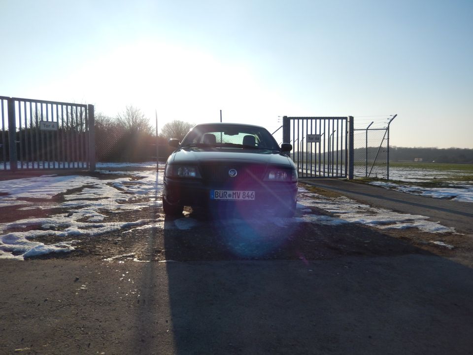 Black sedan parked in front of a closed gate with snow on the ground
