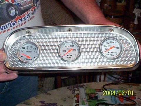 1963 Ford Falcon - A person holds a chrome gauge cluster with three dials, including volts, oil pressure, and water temperature.