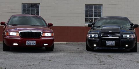 2003 Ford Crown Victoria - maroon Mercury Grand Marquis with EVIL MGM plate parked beside a black Ford Crown Victoria with push bar and EVIL VIC plate.