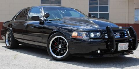 2003 Ford Crown Victoria - glossy black Ford Crown Victoria sedan fitted with a brush guard, blacked-out wheels and an EVIL VIC license plate, parked on pavement.