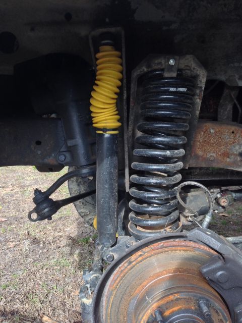 1979 Ford Bronco - Close-up view of the front suspension system, revealing a yellow shock absorber and a black coil spring.