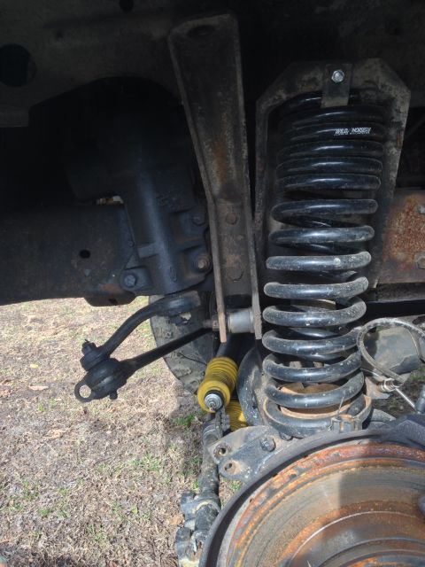 1979 Ford Bronco - Close-up of a vehicle's front suspension system, a coil spring and yellow shock absorber. The Supermotors.net logo is present in the lower…