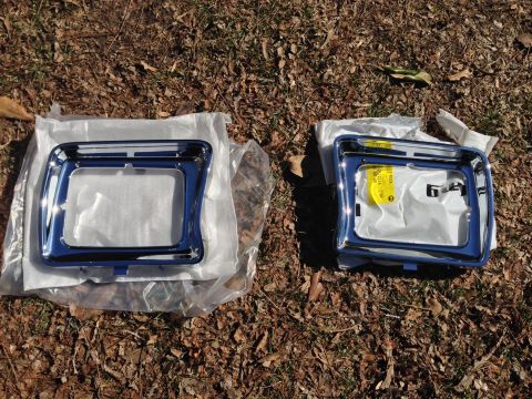 1979 Ford Bronco - Two chrome headlight bezels are displayed on the ground, one a yellow identification tag.