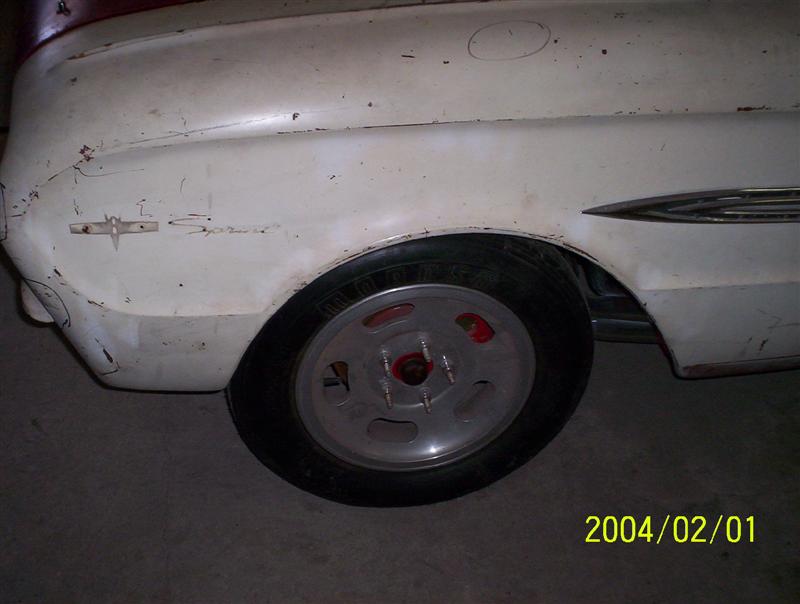 White 1963 Ford Falcon fender with chrome trim and a silver wheel. The car shows signs of wear