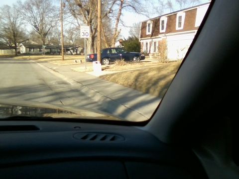 1995 Mercury Grand Marquis - A dark sedan is parked on a residential street next to a house. A speed limit sign is visible.