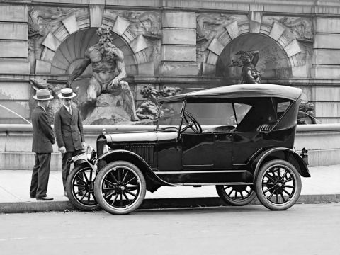 1909 Ford Model T - A touring car from the mid-1920s is parked on a street, with two men in formal attire observing it.