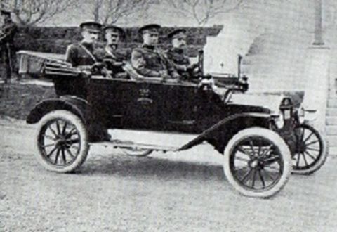 1915 Ford Model T - A dark touring car carries four men in uniform, viewed from the front-right angle.