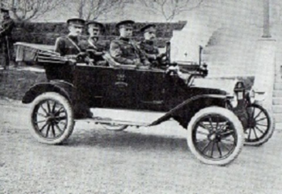 Dark touring car with four men in uniform, seen from the front-right