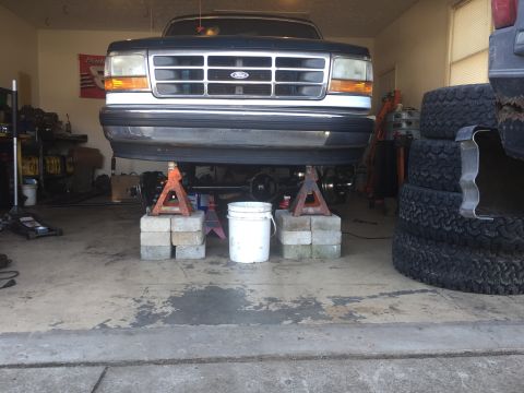 1994 Ford Bronco - A Ford truck is raised on jack stands in a garage, showing its front end and undercarriage.