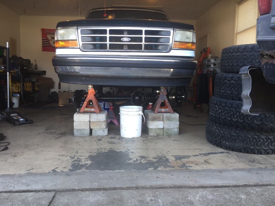 Front view of a Ford F-Series truck on jack stands in a garage. Grille and headlights visible