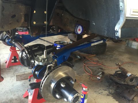 1994 Ford Bronco - Close-up of a vehicle's front axle and suspension components being worked on in a garage.