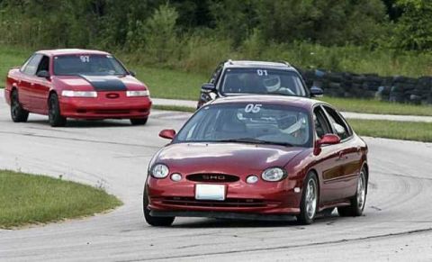 1997 Ford Taurus - Two sedans race on a track, one with a black stripe on the hood and the number 97 on its windshield.