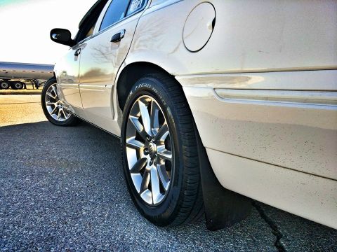 2000 Mercury Grand Marquis - A cream-colored 2000 Mercury Grand Marquis sedan is viewed from the side, focusing on the rear wheel and fender area behind the front wheel.
