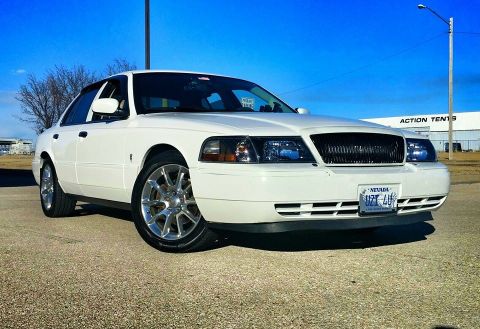 2000 Mercury Grand Marquis - White 2000 Mercury Grand Marquis with aftermarket wheels parked on gravel under a clear blue sky.