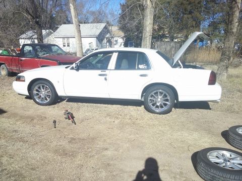 2000 Mercury Grand Marquis - A white 2000 Mercury Grand Marquis is parked outdoors with its trunk open, next to a red pickup truck.