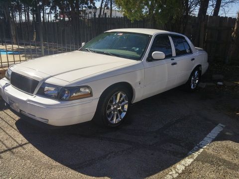 2000 Mercury Grand Marquis - White 2000 Mercury Grand Marquis sedan parked on asphalt with a fence and trees in the background.