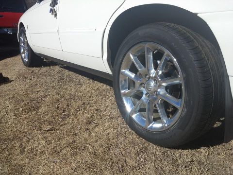 2000 Mercury Grand Marquis - The side profile of a white sedan is shown, with a focus on its chrome wheels and the dry grass beneath it.