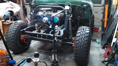 1967 Ford F-250 - Front view of a green truck chassis with its engine exposed and large off-road tires, in a workshop setting.
