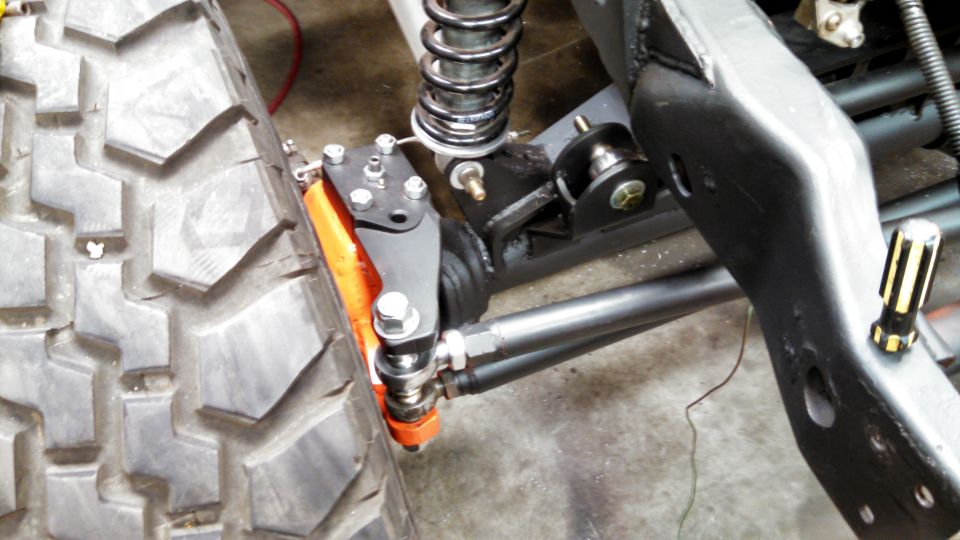 Close-up of a large off-road tire and suspension parts, including a shock absorber and steering linkage