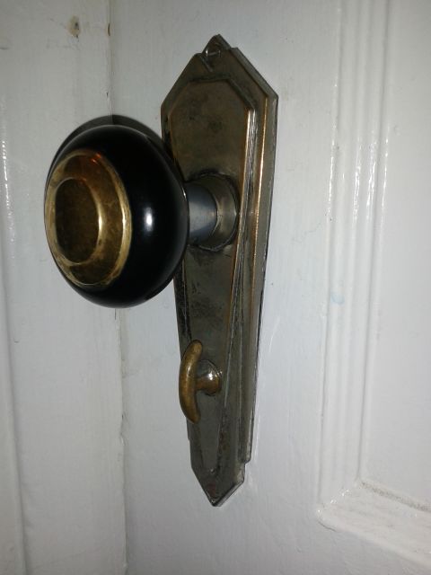 1990 Ford Bronco - A close-up view of an antique black and brass door knob mounted on a decorative metal plate against a white door.