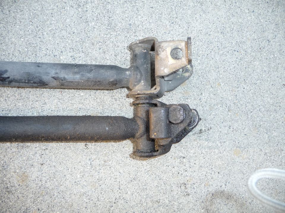 Two black car suspension rods with metal brackets attached, resting on a concrete surface