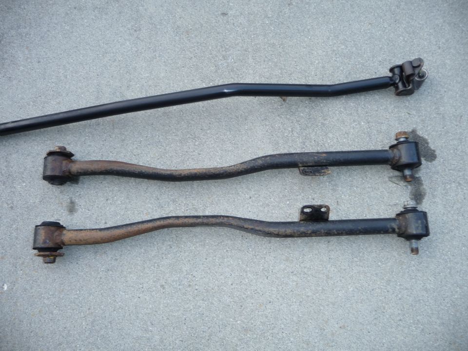 Three automotive suspension control arms laid out on a concrete surface