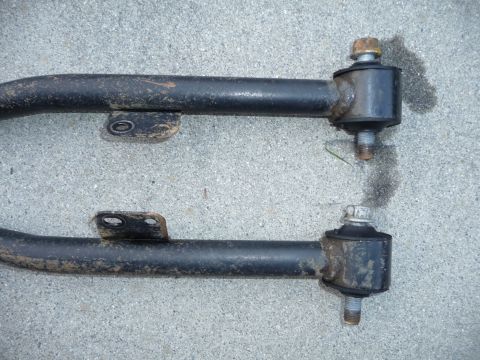 1993 Mazda MX-3 - Close-up of two dirty suspension control arms, showing their mounting points and hardware.