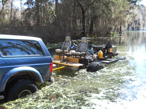 1992 Ford Bronco - A blue 1992 Ford Bronco is partially submerged in swampy water, connected to a custom-built amphibious vehicle.
