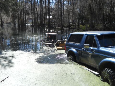 1992 Ford Bronco - A blue SUV navigates through a swampy area, with a makeshift platform carrying equipment visible in the water.