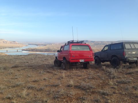1979 Ford Bronco - Two SUVs, including a red 1979 Ford Bronco, are parked on a hill overlooking a river valley.
