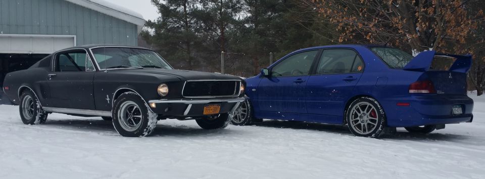 1968 Ford Mustang parked next to a blue Mitsubishi Lancer Evolution in the snow